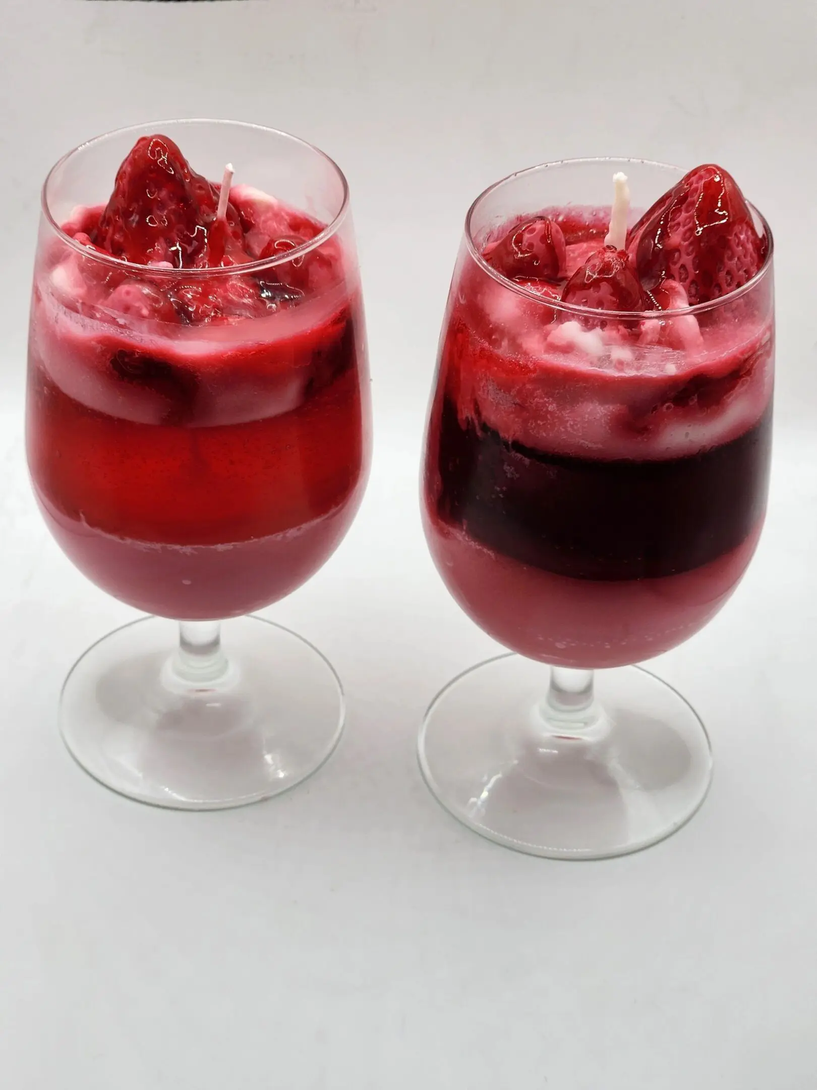 Two glasses of red wine with strawberries in them.