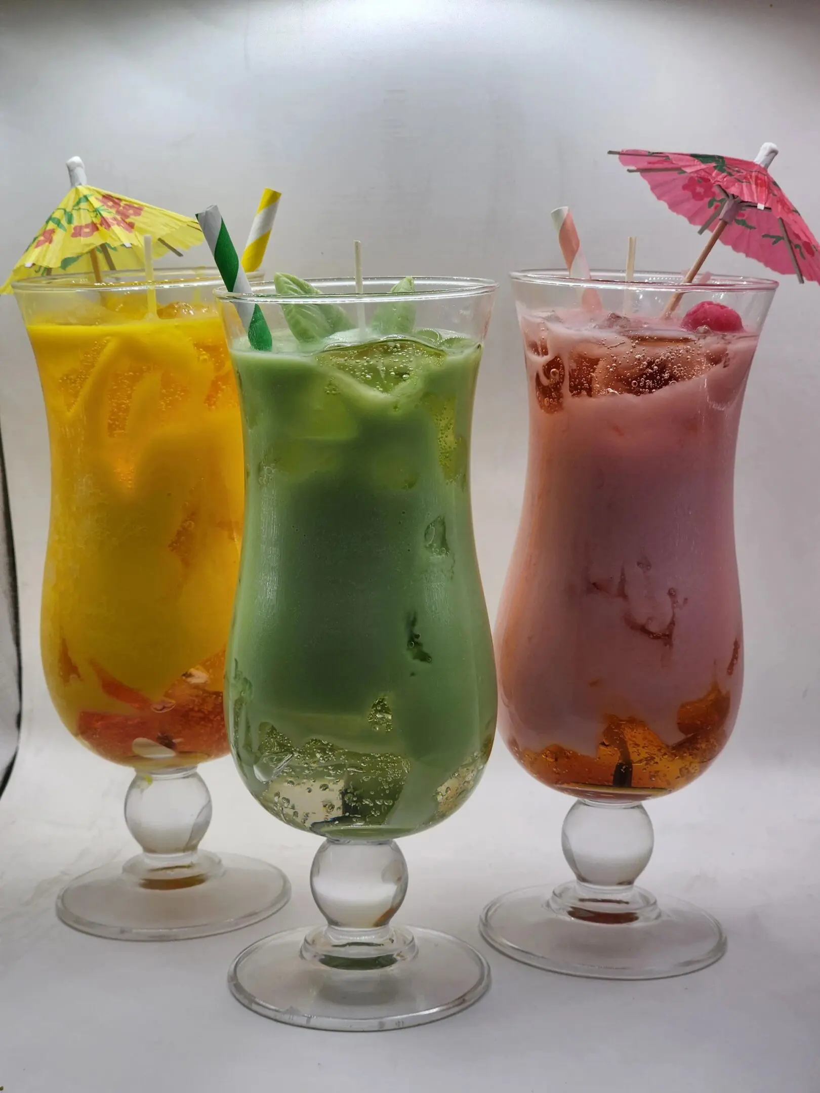 Three glasses of different drinks with umbrellas on them.