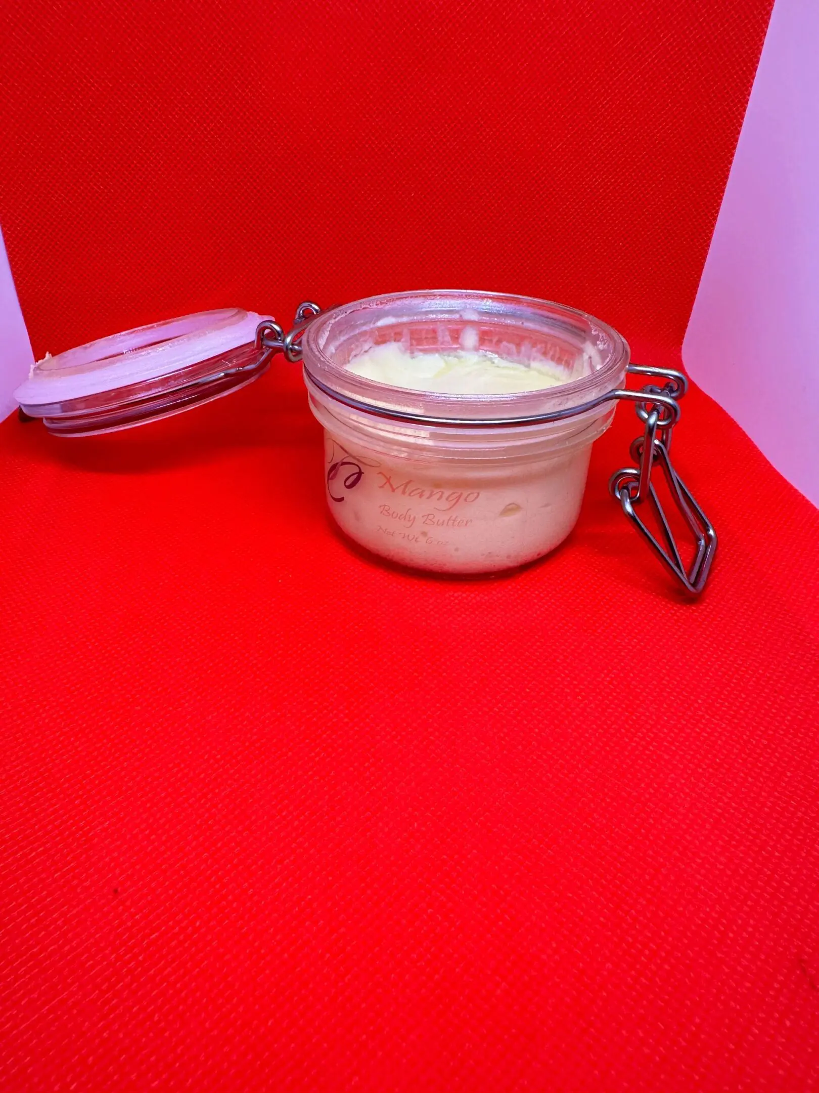 A jar of body butter sitting on top of a red table.